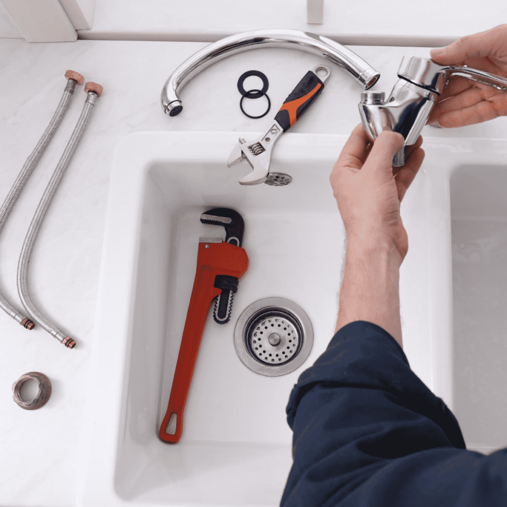 man holding the uninstalled parts of a kitchen sink faucet with tools on the counter next to him
