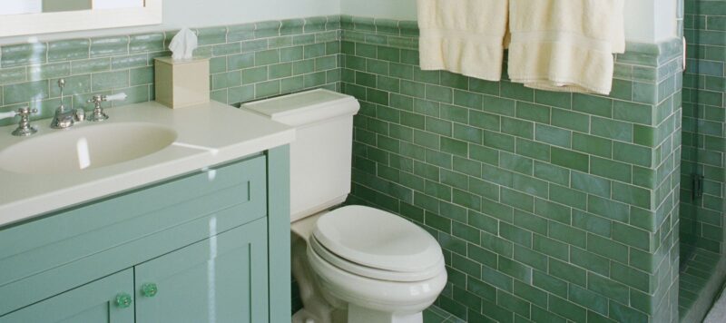 a white toilet in a residential bathroom with green walls and green cabinets