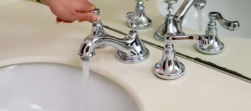 a woman turning a handle to turn on a bathroom sink faucet