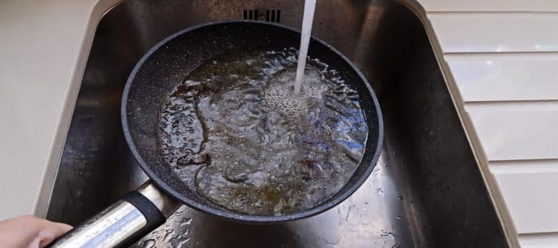 pan full of grease being filled with water in a kitchen sink