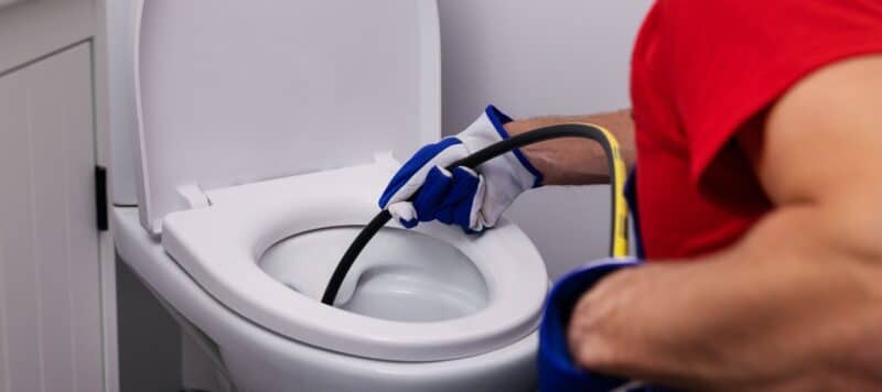 plumbing wearing gloves while feeding a thin black drain tube into toilet