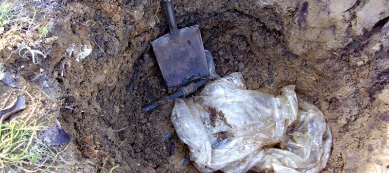 closeup of a hole being dug to find a water leak in an underground pipe, shovel and plastic bag in the hole