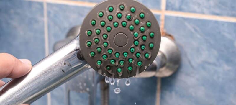 A close-up of a showerhead with low water pressure and leaking water droplets