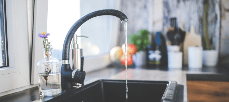 closeup of a water faucet in the kitchen running with water